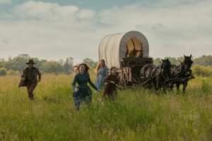 "People run around joyfully with a wagon in the distance. "