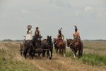 "People in a wagon pass people on horseback. "