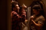 "Two young men excitedly hold cash in a dimly lit closet, with clothes hanging in the background and an open safe visible behind them, suggesting they just found or stole the money."