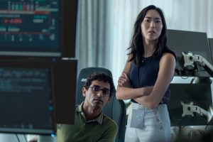 "A man and woman in a modern office intently looking at computer screens displaying data, with chairs and equipment visible in the background, suggesting a tech or research environment."