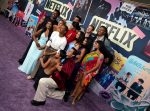 "Group of people posing together on a purple carpet at a Netflix event, with colorful posters and Netflix logos in the background, creating a lively and festive atmosphere."