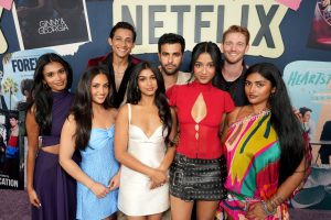 "A group of young adults posing together at a Netflix event, standing in front of a backdrop with Netflix branding and various show posters, dressed in colorful, stylish outfits."