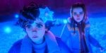 "Two animated characters, one with a glowing blue flower on their head, stand in a mysterious, glowing blue-lit environment with floating orbs and an atmosphere of surprise or concern."