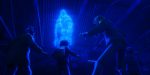 "Four people in winter clothes face a glowing blue ghostly figure hovering inside a dark, abandoned wooden building, illuminated by eerie blue light."