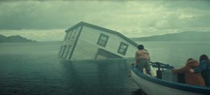 "A partially submerged house tilts in a misty lake as three people in a small boat observe, with cloudy skies and distant hills creating a dramatic, mysterious atmosphere."